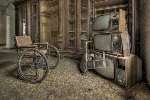 An old ivalid wheelchair and old televisions in an old building