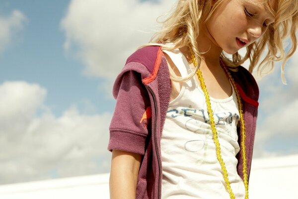 Fille blonde avec des perles jaunes sur le cou sur fond de ciel nuageux