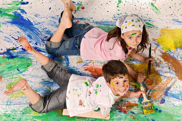 A boy and a girl paint with brushes on the canvas