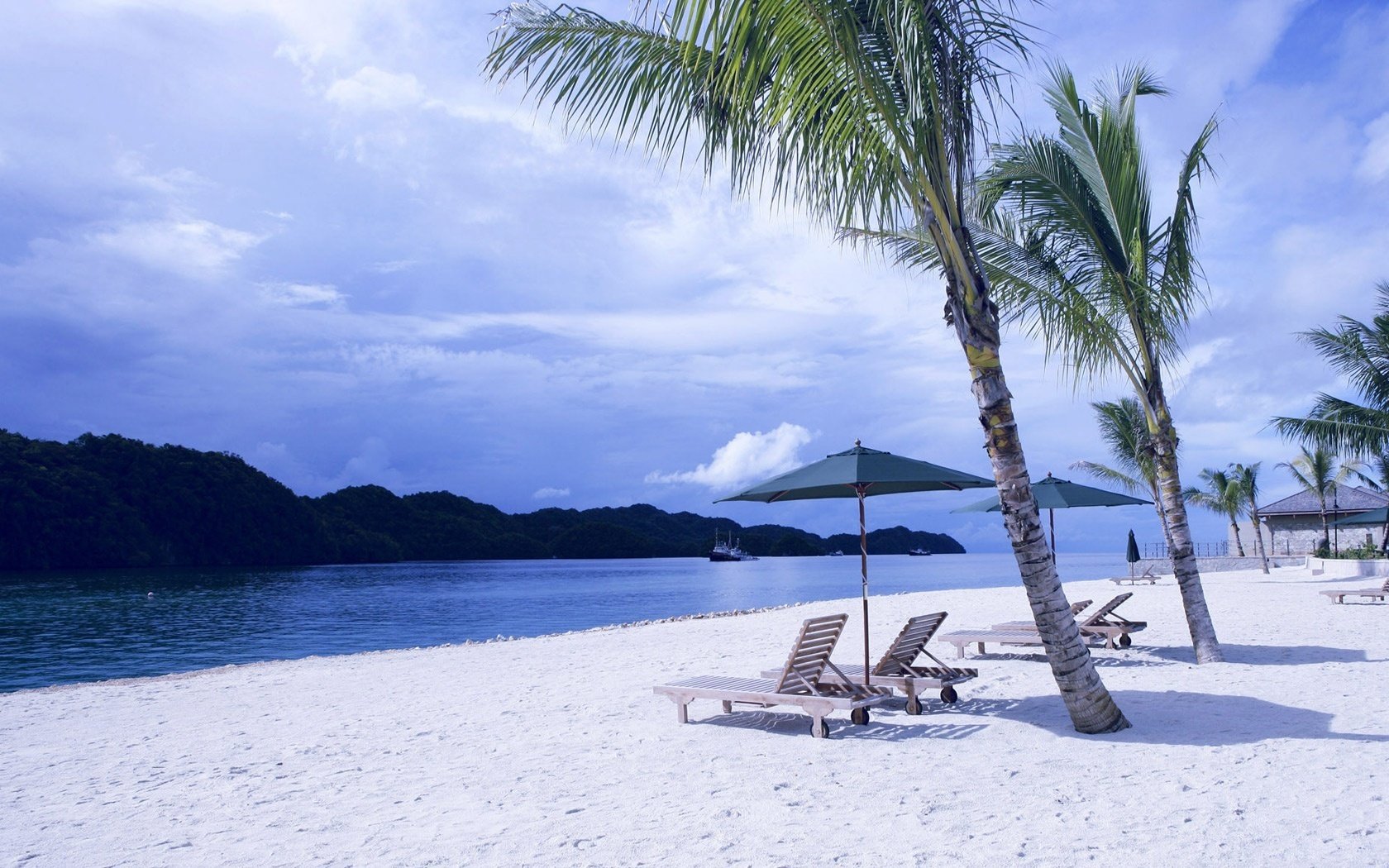 empty beach wooden deck chairs rocks beach water the sky palm trees sunbeds sun loungers umbrellas mountains shore vacation stay resort islands tropics clouds shadow summer