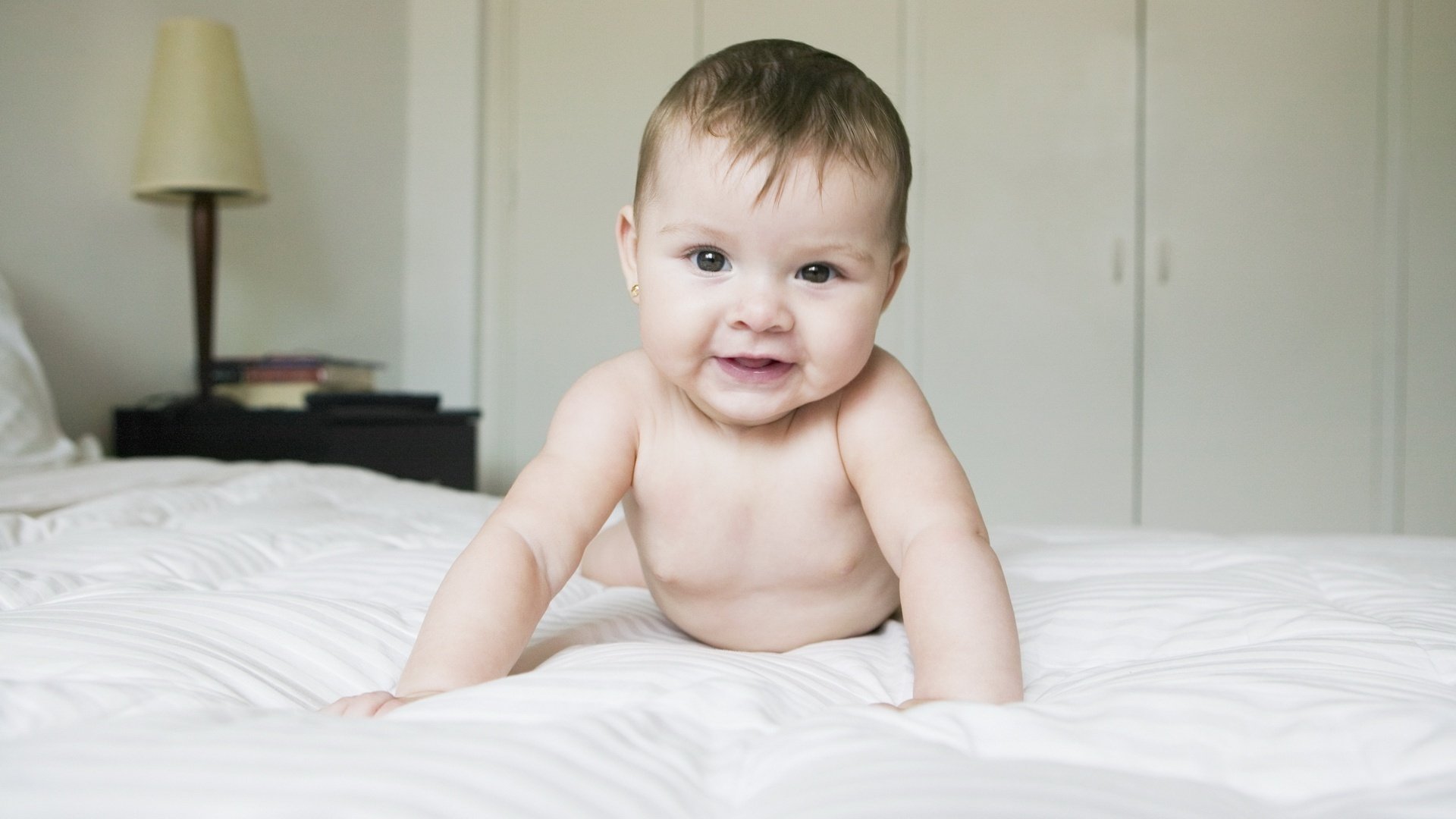 pelo esponjoso aquí estoy ojos oscuros retrato mirada cara ojos sonrisa cama cama habitación lámpara de pie libros bebé migaja bebé gateo desnudo