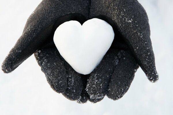 A white heart made of snow in the palms of your hands