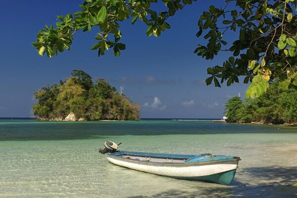 Barca sull acqua di mare trasparente vicino alla riva su uno sfondo di cielo blu e vegetazione verde