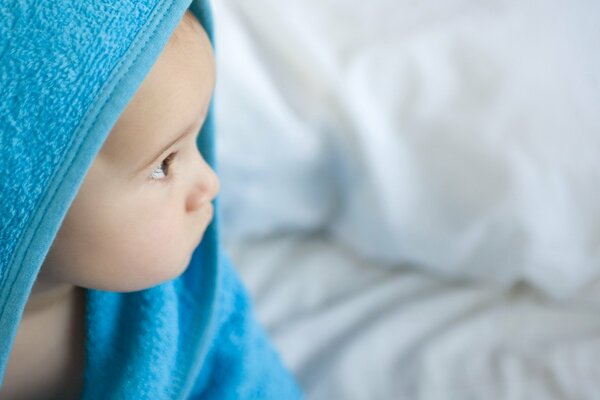 Dziecko po kąpieli siedzi w niebieskim ręczniku