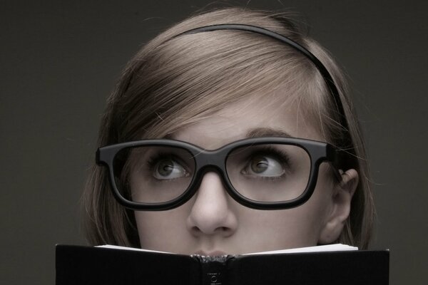 A thoughtful girl with glasses behind a book