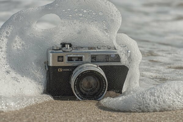 Eine Kamera im Sand, die mit einer Welle weggespült wird