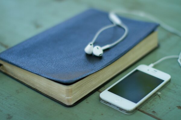 Ein iPhone mit Kopfhörern und einem blauen Buch in der Nähe