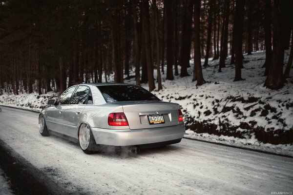 Auténtico coche Audi blanco entre el bosque cubierto de nieve y la carretera