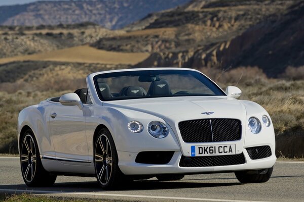 There is a white Bentley on the road among the mountains