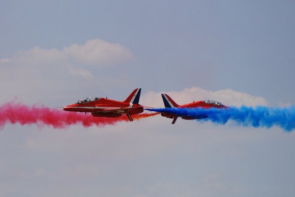 Два самолета летят с красным и синим дымом