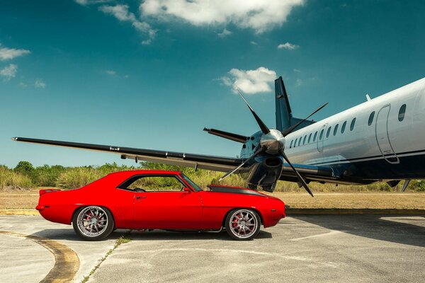 Bright red chevrolet near the plane