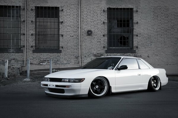 Coche nissan Silvia S13 blanco en una pared de ladrillo con ventanas en rejillas