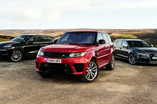 Trois voitures audi, porsche, land rover, range rover sur le terrain