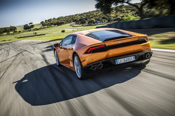 An orange-colored Lamborghini is racing along the highway