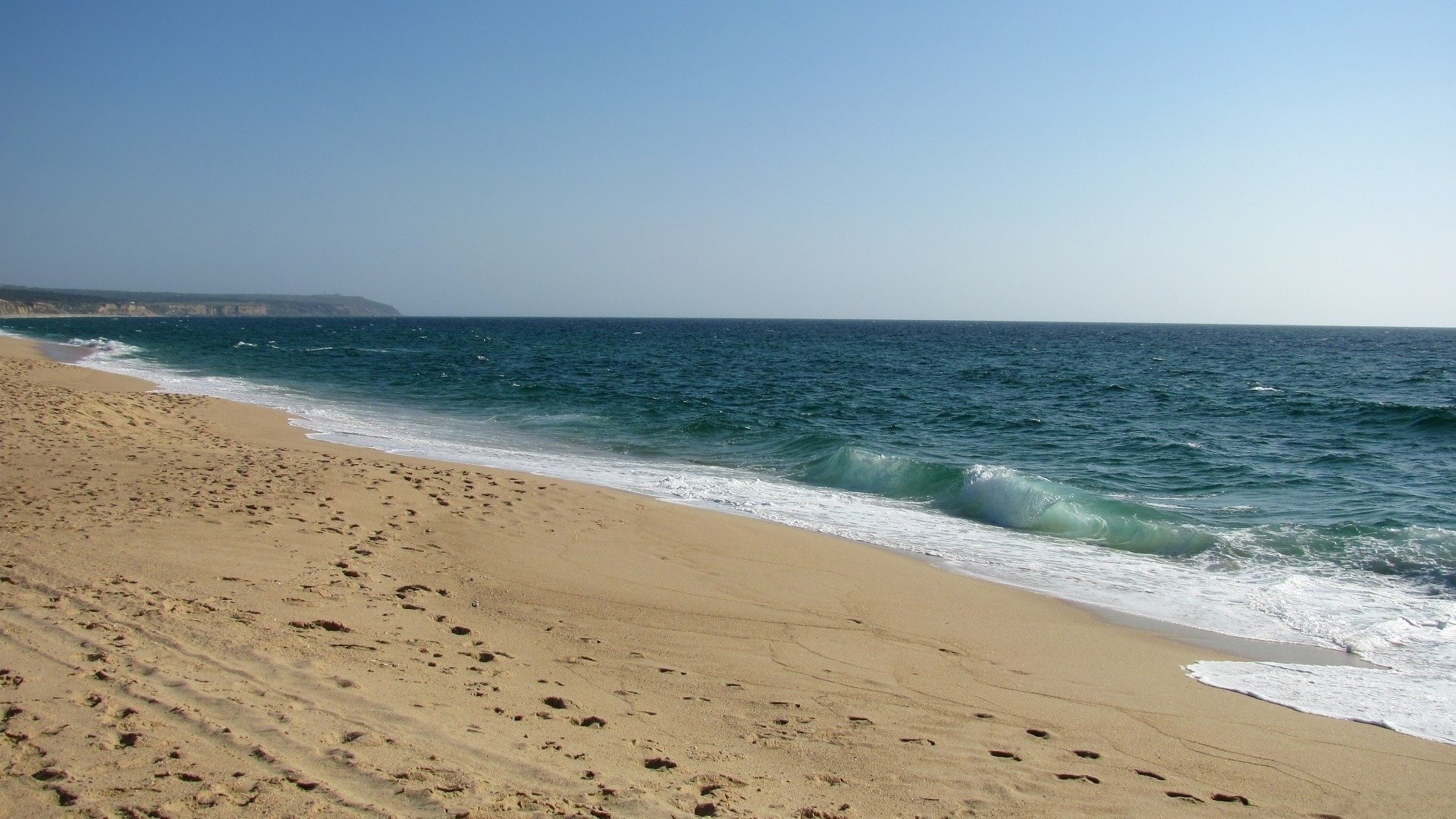 ea splash shore land ocean surf waves spray water foam breeze shore coast coast land sand footprints calm calm sky sky smooth surface horizon beach