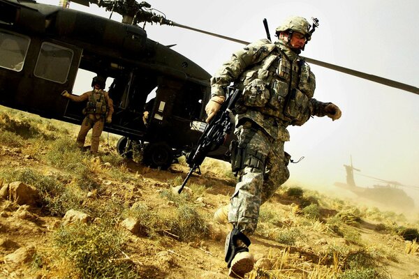 Militärmann mit Maschinengewehr auf dem Hintergrund eines Hubschraubers in der Mitte des Feldes