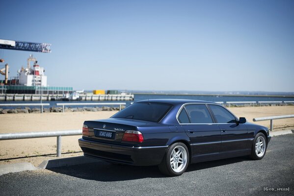 BMW E38 740il negro estacionado cerca de la playa vista lateral contra el mar y las estructuras portuarias