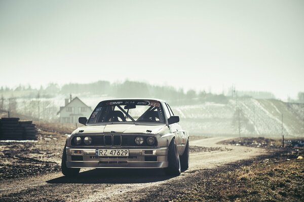 Voiture BMW E30 argent dans les rayons du soleil sur la route