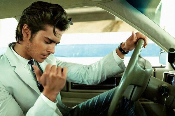 A handsome man in a shirt is sitting in a car