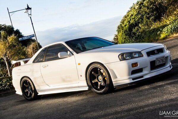 Image of a white sports car against the background of the horizon and the greenery of trees