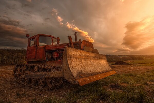 A bulldozer in a field against a threatening sky