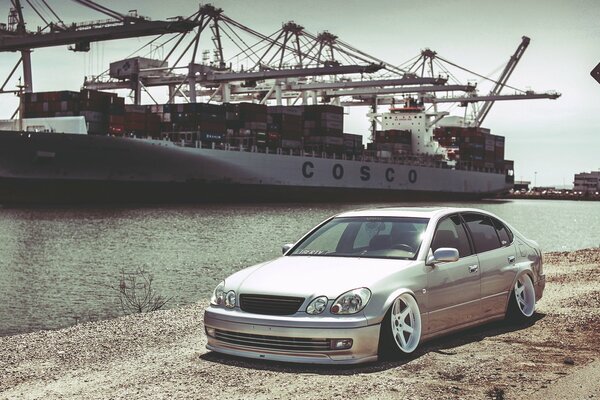 Lexus is standing on the riverbank, and behind a large ship