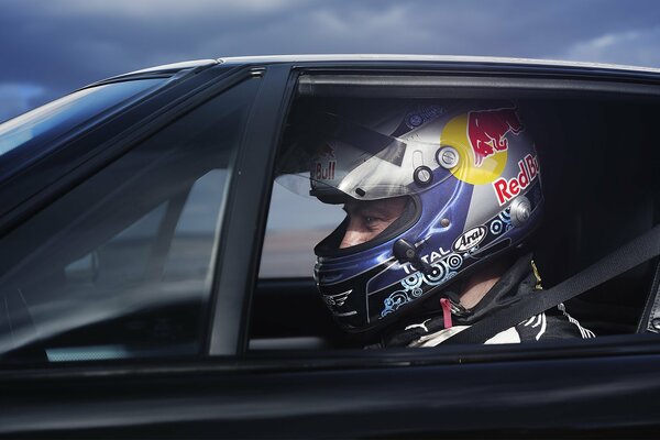 A pilot in a car wearing a helmet with a red bull