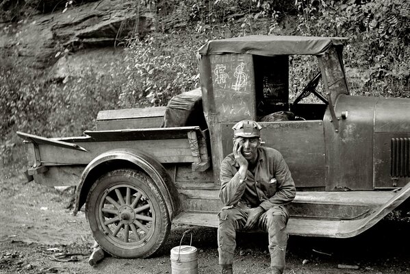 Black and white photo of a worker resting near a truck