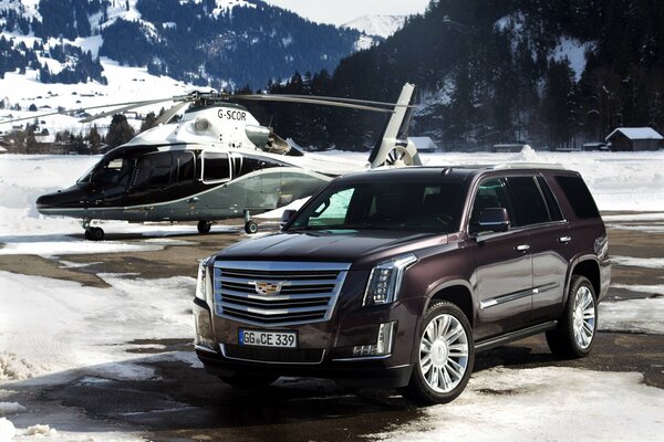 Cadillac and helicopter on snowy mountain landscape