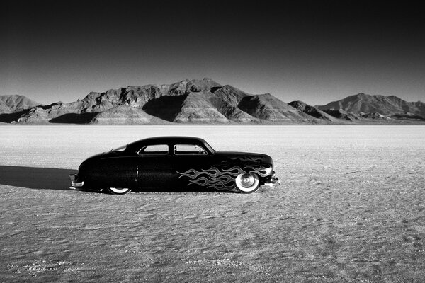 Photo en noir et blanc avec une voiture de course sur fond de montagnes