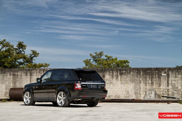 Range Rover auf dem Parkplatz an einem alten Zaun und rostigen Rohren