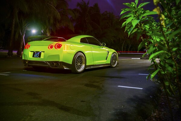 A green Nissan with its taillights on, standing on the asphalt