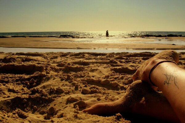 Beine mit Tattoo am Strand unter einem romantischen Sonnenuntergang