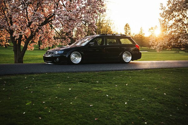 Black Subaru with white wheels on a sunny day