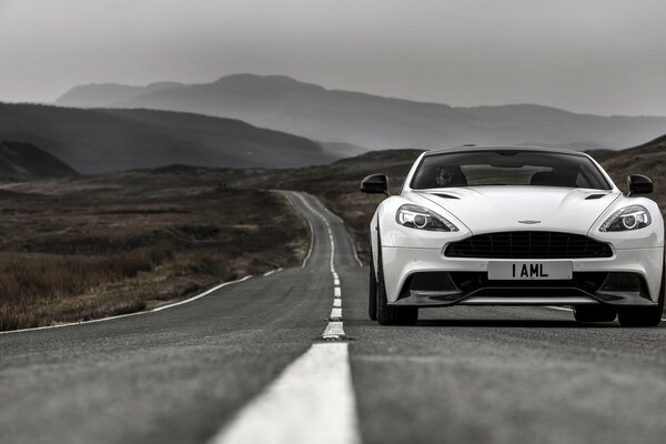 Una Aston Martin bianca cavalca una strada senza fine tra le montagne