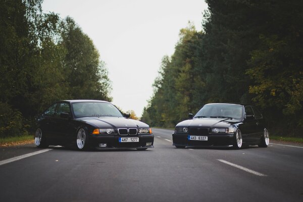 Voitures BMW M3 E36 3 série oldschool tuning debout à travers la route goudronnée sur fond de forêt vue de face