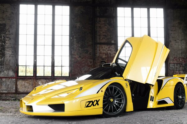 A yellow Ferrari with an open door stands in a building with windows