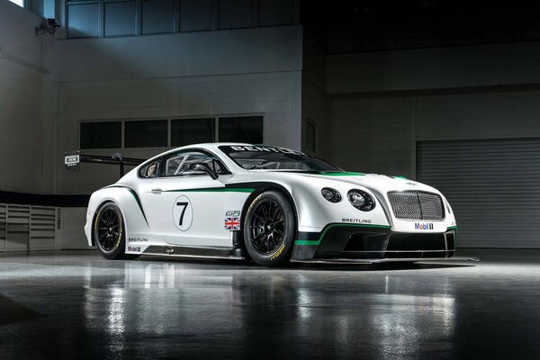 A white Bentley car is parked on the asphalt near the building