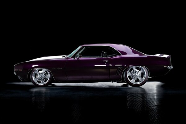 Purple Chevrolet with gray wheels standing sideways in a dark room