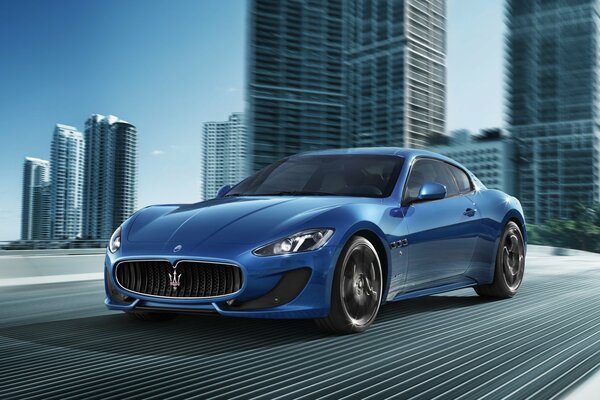 Niebieski samochód firmy Maserati pędzi przez most nowoczesnego miasta