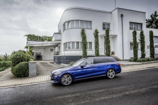 Kobalt-Mercedes-Benz auf dem Hintergrund eines weißen zweistöckigen Hauses