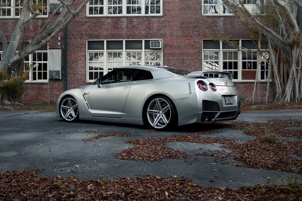 A gray nissan standing on the asphalt near a brick building