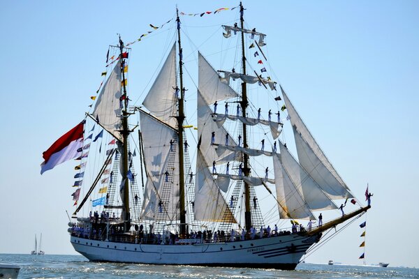 A sailing ship with people on it in the sea against a clear blue sky