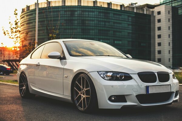 Voiture blanche BMW sur fond de bâtiment sur la route au coucher du soleil