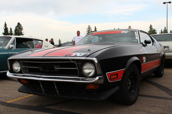 A black car with red stripes is parked in the parking lot