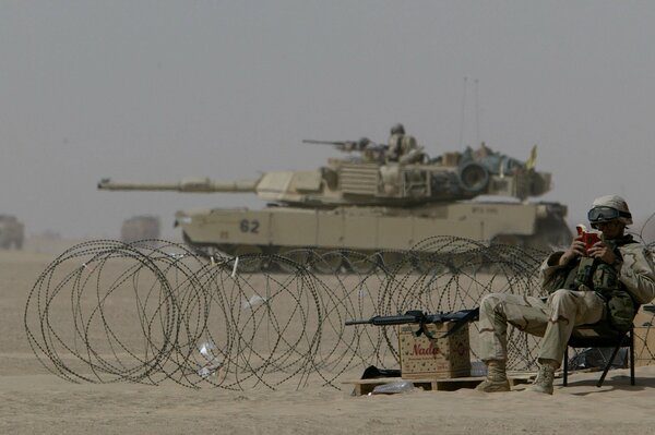 Żołnierz spokojnie czyta książkę na tle działającego czołgu