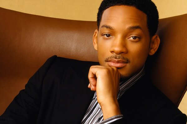 Actor Will Smith is sitting in a brown armchair