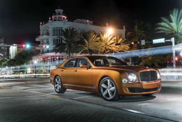 An orange Bentley in the middle of a night city