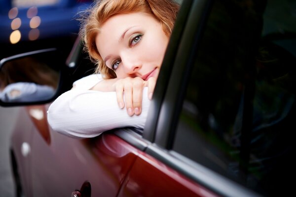 The girl in the car. The red car. A car and a girl. The girl looks at you from the car