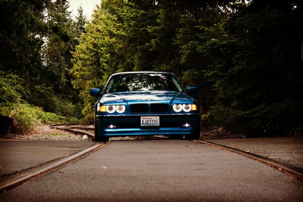 Une bmw E38 bleue teintée avec des phares cool roule sur une route de campagne